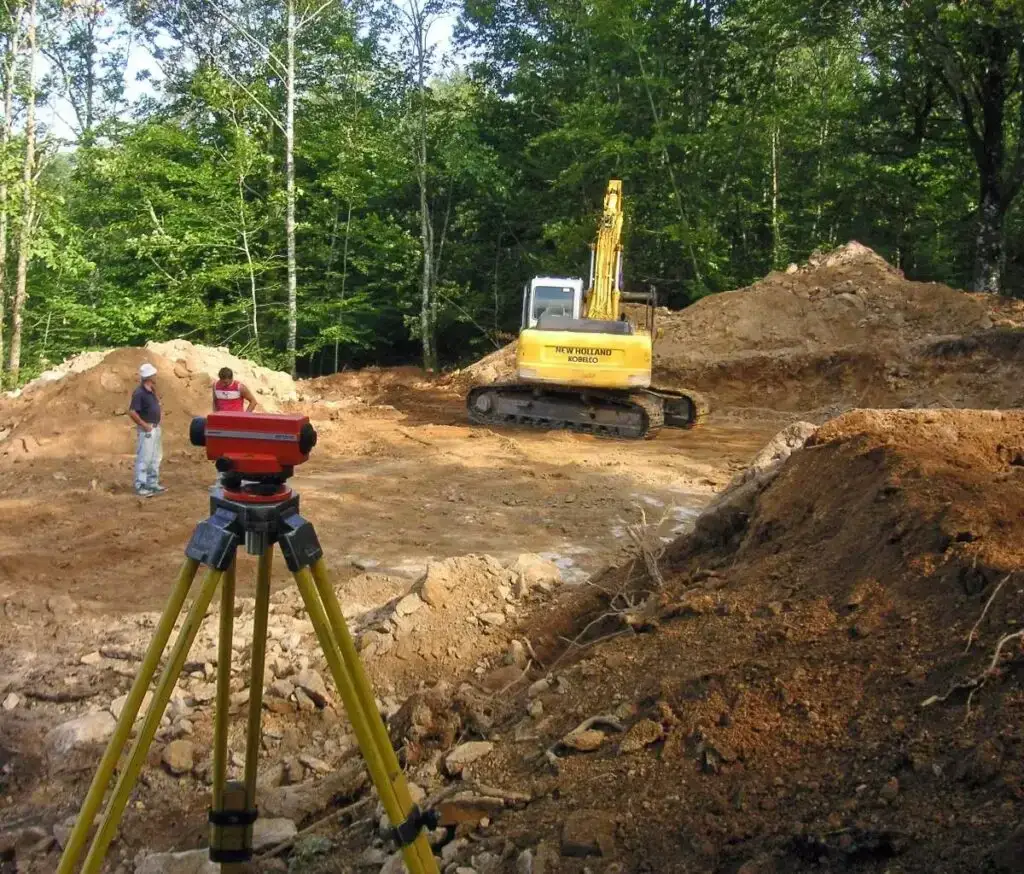 Three men standing next to an excavator doing site survey with a theodolite
